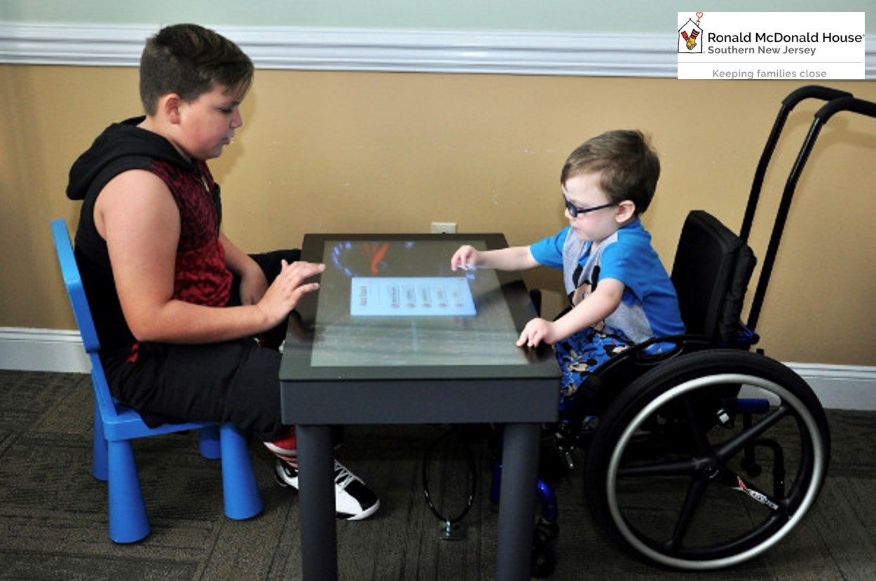Two people using an interactive table, including a wheelchair user, at Ronald McDonald House Southern New Jersey