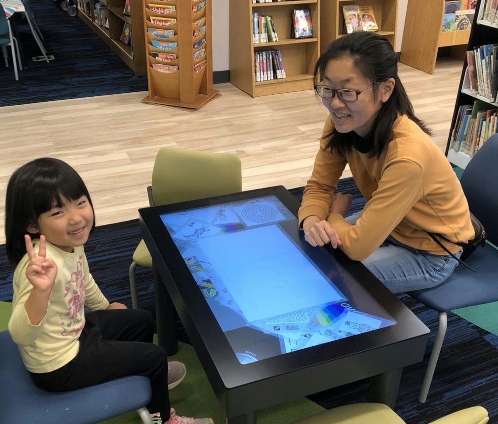 A child and adult beside a table running Paint’Touch